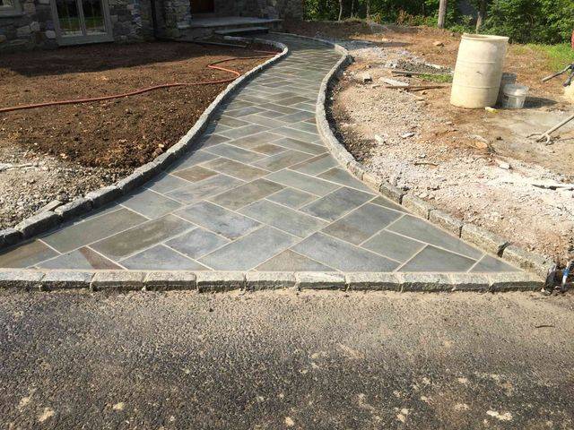 A herringbone paver walkway with a cobblestone border leading to a house
