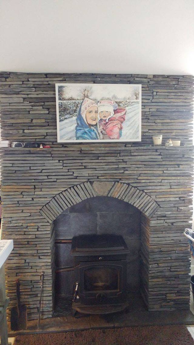 A stone fireplace with a cast iron stove and a framed portrait on the mantel