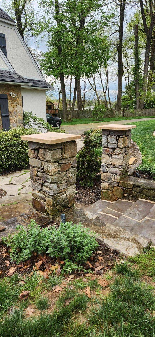 Two square stone pillars with stone caps flanking a walkway toward a house